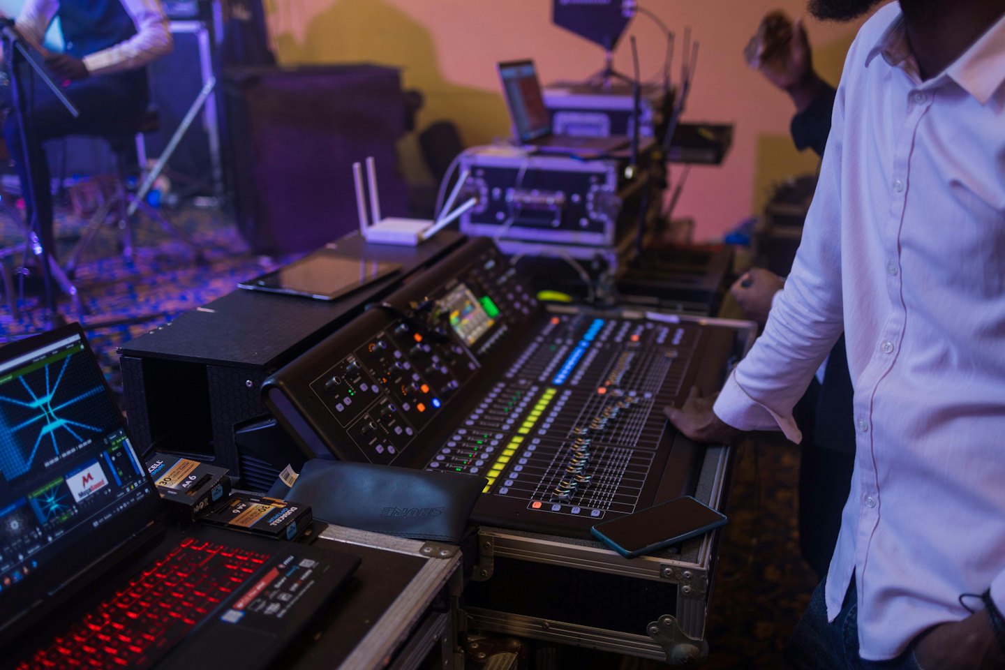 Sound engineer adjusts audio mixing console with laptops and equipment.