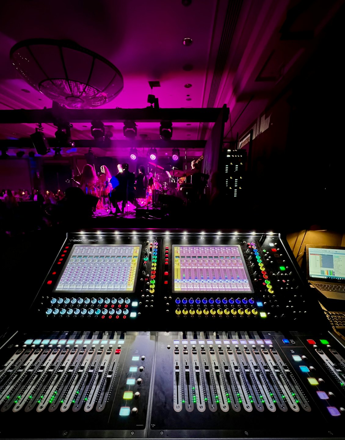 Sound engineering console with illuminated screens and band performing.