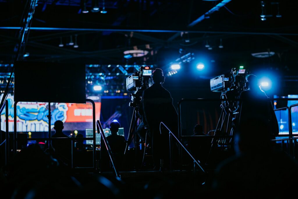 Professionals operate cameras at a dimly lit event with blue stage lighting.
